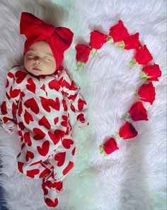 a baby laying on top of a white blanket next to red rose petals and a heart