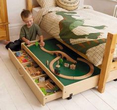 a young boy playing with his toy train set on the floor in front of a bed