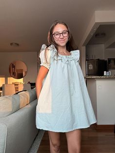 a woman standing in front of a couch wearing glasses and a blue checkered dress