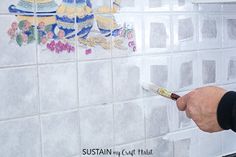 a person is using a brush to paint the tile on a wall in a kitchen