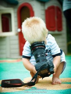 a small child with a camera and a bird on the ground in front of him