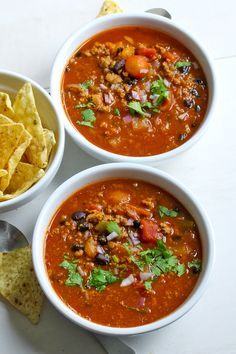 three bowls of chili with tortilla chips on the side