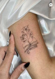 a woman's arm with a book and flowers tattoo on it