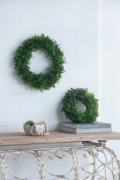 two green wreaths sitting on top of a wooden table next to a white brick wall