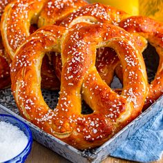 some pretzels are sitting in a tin on a table next to beer and salt