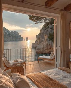 a bedroom with a view of the ocean and cliffs at sunset or sunrise, in front of an open door that leads to a balcony