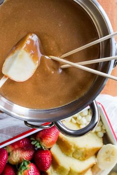 a pot filled with chocolate and bananas on top of a wooden table next to other foods