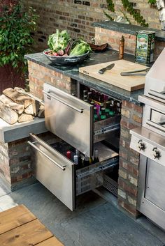 an outdoor kitchen with stainless steel appliances and grilling materials on the counter top, surrounded by brick walls