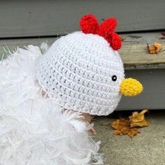 a white crocheted chicken hat with red and yellow feathers on it's head