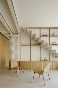 two chairs and a table in a room with wooden shelves on the wall behind them