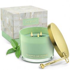 a green candle sitting in front of a box with mint leaves on the side and a gold lid