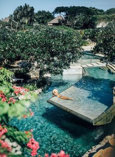 an outdoor swimming pool surrounded by greenery and trees with a person floating in it