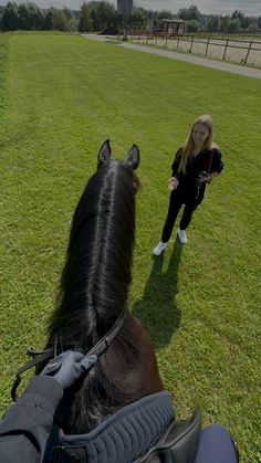 a woman standing next to a brown horse on top of a lush green field