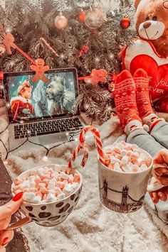 two people are eating marshmallows in front of a christmas tree with a laptop