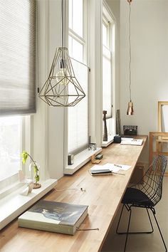 a long table with some books on it in front of two windows and a lamp hanging from the ceiling