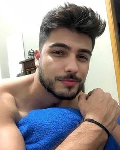 a shirtless man in a blue towel looking at the camera with his hand on his chest