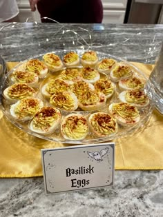 an assortment of deviled eggs on a glass platter with a sign that says basilisk eggs