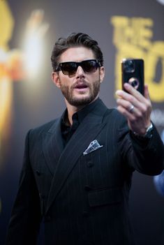 a man in a suit taking a selfie with his cell phone while wearing sunglasses