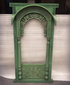 an old green wooden arch with carvings on the top and bottom, in front of a white wall