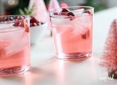 two glasses filled with ice and cherries on top of a white table next to a bowl of berries