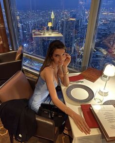 a woman sitting at a table in front of a window with a view of the city