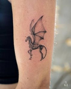 a black and white photo of a dragon tattoo on the right arm, with wings spread out