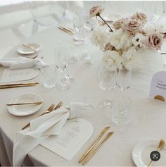 the table is set with white and gold place settings, napkins, and flowers