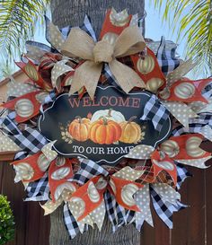 a welcome to our home wreath with pumpkins and gingham ribbon hanging on a tree