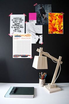 a desk topped with a lamp next to a pile of papers and pictures on the wall