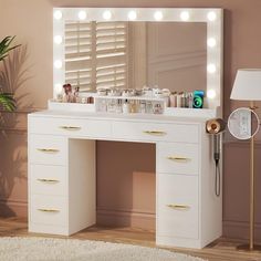 a white vanity with lights on it and a mirror in front of it, next to a plant