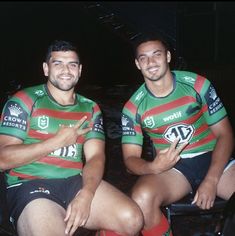 two men sitting next to each other wearing green and red striped jerseys with their arms crossed