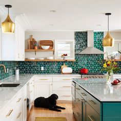 a black dog laying on the floor in a kitchen with white cabinets and green backsplash