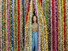 a woman standing in front of a wall covered with multicolored streamers and beads