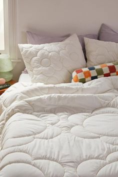 an unmade bed with white comforter and pillows on the headboard in front of a window