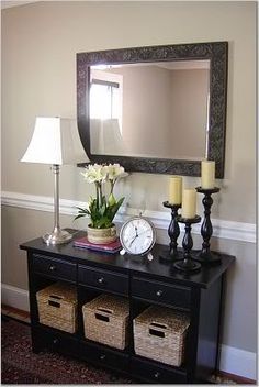 a black dresser with two baskets under it and a mirror on the wall behind it