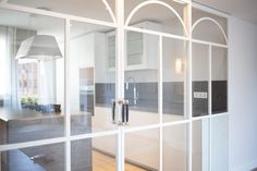 an open glass door leading to a kitchen and dining room with white walls, wood flooring and large windows