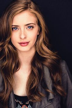 a woman with long brown hair and blue eyes posing for a photo in front of a black background