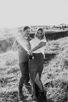 a man and woman are standing in the grass with their arms around each other while spraying water on them