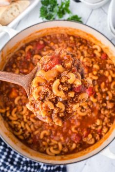 a ladle full of chili macaroni and cheese being held by a wooden spoon