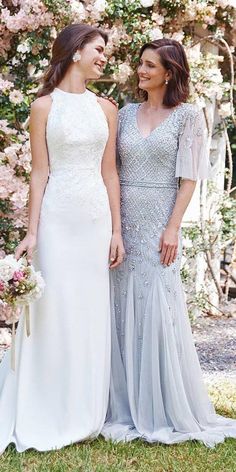 two women standing next to each other in front of some bushes and trees with pink flowers