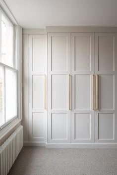 an empty room with white cupboards and a radiator next to the window