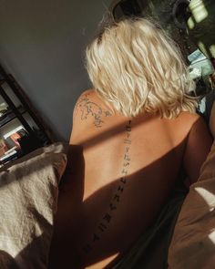 a woman laying in bed with her back turned to the camera and tattoos on her chest