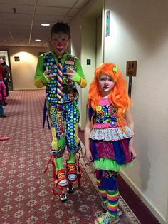 two children in clown costumes are walking down the hallway with one holding a cell phone