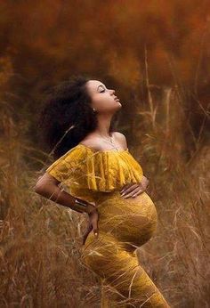 a pregnant woman standing in tall grass with her hands on her hips and looking up