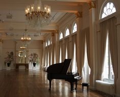 a grand piano in the middle of a large room with chandeliers and windows