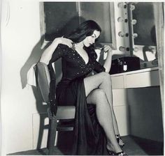 black and white photograph of a woman in fishnet stockings sitting on a chair looking at her cell phone