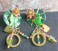 "A fabulous vintage pair of Lunch at the Ritz pierced earrings. These stunning earrings feature green frogs with orange eyes. The frogs are shown sitting on green and gold striped lily pads. The lily pads include lovely blooming pink flowers with beautiful sparkling Swarovski crystals. Gold hearts, green and purple Swarovski crystals, striking Austrian beads complete the design of these earrings. Both are 24K gold electroplated with 14K gold posts. Each earring is signed \"Lunch at the Ritz.\" a Frog On Lilypad, The Ritz, Gold Stripes, Stunning Earrings, Etsy Shipping, Lily Pads, Pretty Jewellery, Frogs, Earings Piercings