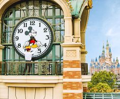 a large clock on the side of a building with a castle in the back ground