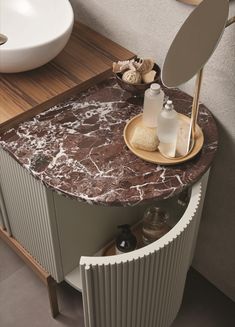 a bathroom vanity with marble counter top and round mirror on the wall above it, next to a white sink