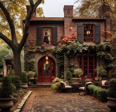 an old brick house with red doors and shutters on the windows is surrounded by greenery